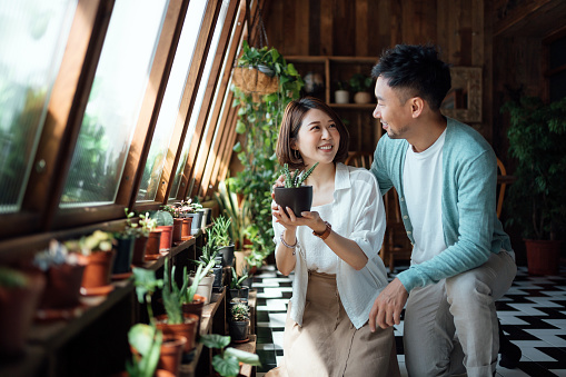 Happy young Asian couple taking care of plants together at balcony at home. Enjoying their time at cozy home. Going green lifestyle