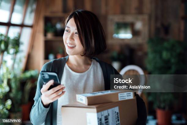 Beautiful Smiling Young Asian Woman With Smartphone Receiving Parcels With Home Delivery Service At Home Online Shopping Mobile Payment Enjoyable Shopping Experience Stock Photo - Download Image Now