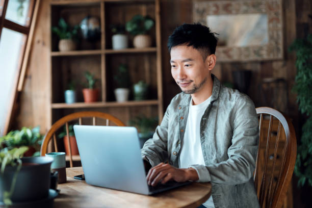 istock Professional young Asian man working from home, using laptop computer in home office. Remote working, freelancer, small business concept 1365749416