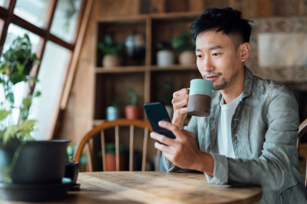 jeune homme asiatique gérant les services bancaires en ligne avec une application mobile sur smartphone, prenant soin de son argent et de ses finances tout en se relaxant à la maison. services bancaires avec la technologie - comptes épargne photos et images de collection