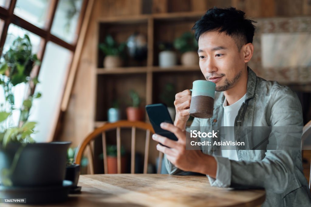 Young Asian man managing online banking with mobile app on smartphone, taking care of his money and finances while relaxing at home. Banking with technology Men Stock Photo