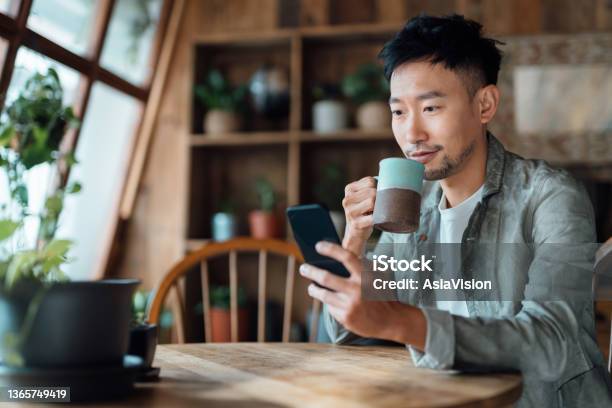 Young Asian Man Managing Online Banking With Mobile App On Smartphone Taking Care Of His Money And Finances While Relaxing At Home Banking With Technology Stock Photo - Download Image Now