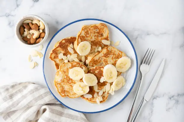 Banana protein pancakes with almond flakes on plate, white marble background, top view