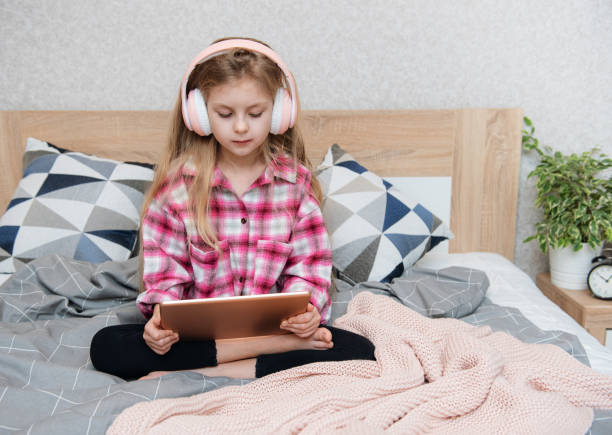 istock Cute Little girl sitting on bed and using tablet at home 1365768282