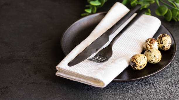 feliz conceito de páscoa. prato de cerâmica preto com talheres, ovos de codorna, guardanapo branco e planta verde para o jantar festivo. cenário de mesa moderno para celebração - eggs animal egg celebration feather - fotografias e filmes do acervo