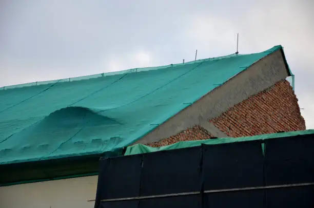 Photo of repair of the roof on the square. building under renovation. pedestrian protection against loose burnt roof tiles on the sidewalk.roof is covered with a green plastic net. historical baroque building