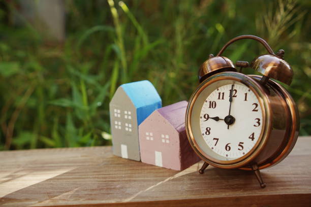istock Alarm clock and house model on table with natural green background 1365773461