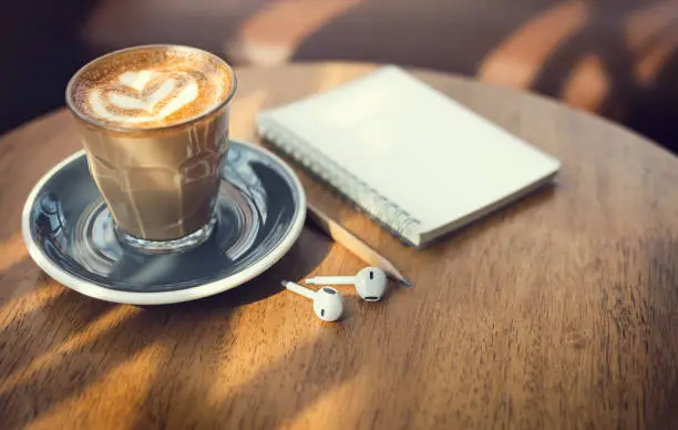 Close-up, latte coffee in old style glass and earphone, note book, pencli on wooden table, vintage tone