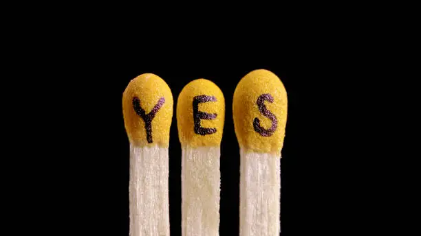 Close-up of three matchsticks with "yes" written on them against black background.