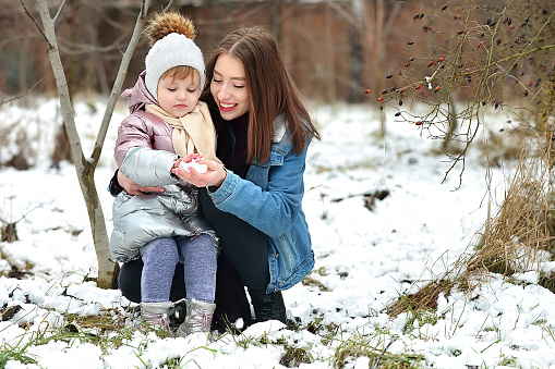 The older sister gives the younger one to touch the snow, winter active walks in winter
