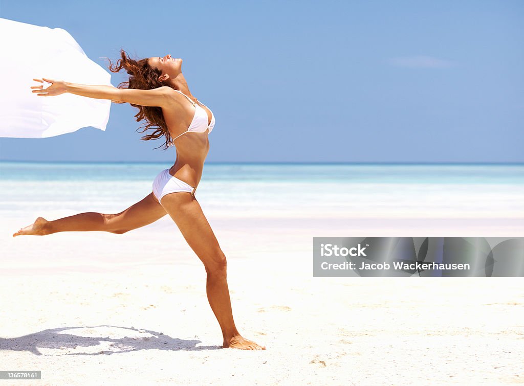 Alive and free! Carefree young woman running with a white sarong along a beach in paradise Beach Stock Photo