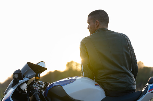 Young man on his motorcycle contemplating the landscape calmly. He is wearing a green leather jacket