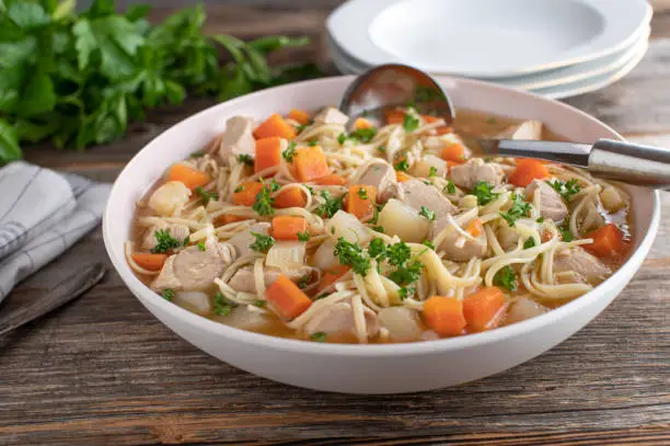 Fresh cooked chicken soup with noodles served as a family meal on rustic and wooden table