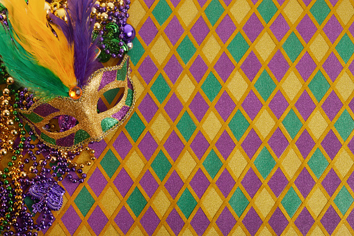 Frame of Mardi Gras Mask and colorful Mardi Gras Beads on diamond shaped background.