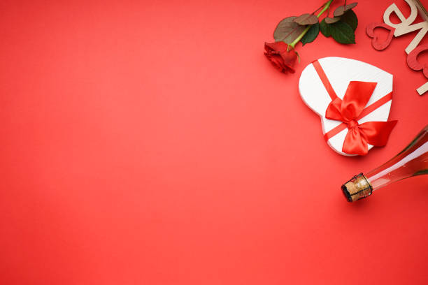 Gift box with champagne for Valentine's Day and roses on a red background, space for text, flat lay.