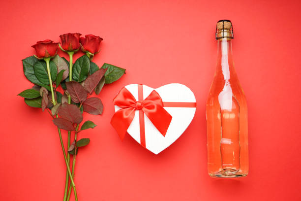 Gift box with champagne for Valentine's Day and roses on a red background, top view.