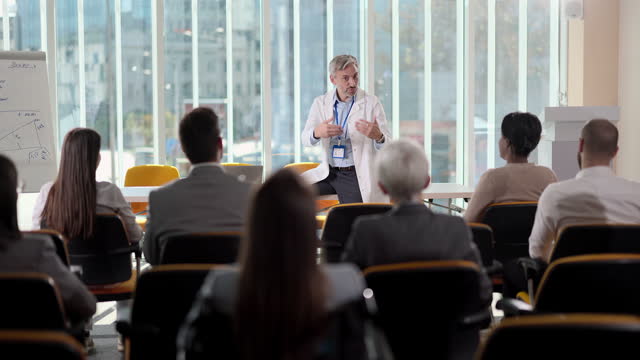 Male doctor talking to large group of people during a medical seminar in hospital.