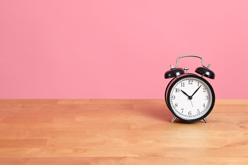 The picture of clock seeting on the desk with pink background.