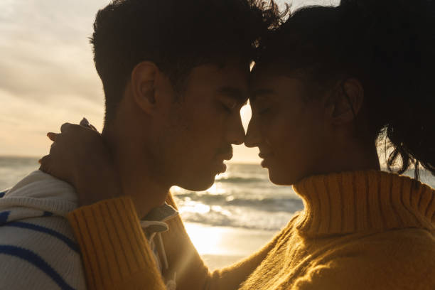 istock Side view of multiracial couple romancing while hugging each other at beach during sunset 1365806158