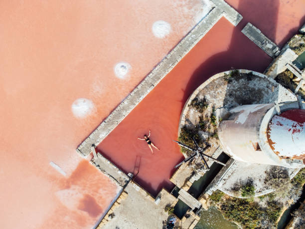 女性はウェルネストリートメントを受けるために塩フラットのピンクの水の中に横たわっている - トラパニ ストックフォトと画像
