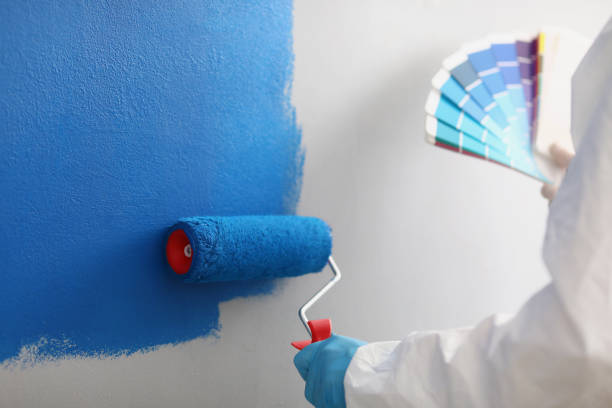 istock Painter with brush tool covered in blue colour painting wall, worker on site 1365807436