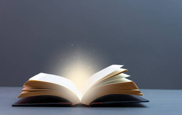 istock Mystery open book with shining light . Fantasy book with magic light  and stars on a table with grey background  and copy space 1365809718