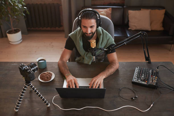 istock Horizontal high angle view shot of modern bearded young Middle Eastern influencer wearing casual clothes sitting at desk alone in loft room using laptop 1365810744