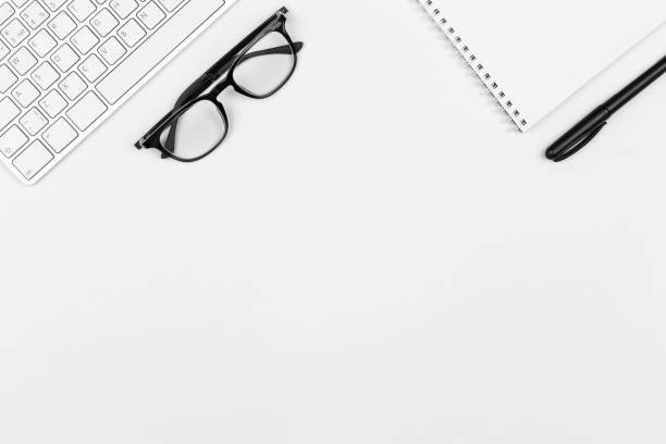 istock Keyboard, black eyeglasses, notepad, pen on white background. Minimal business concept. Office supplies on table. Monochrome workspace. Copy space, flat lay, top view 1365811324