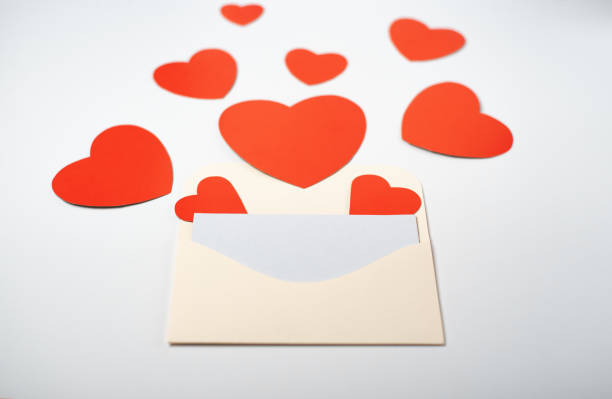 istock Envelope with a blank sheet and red paper hearts on the light (white) background. 1365815237