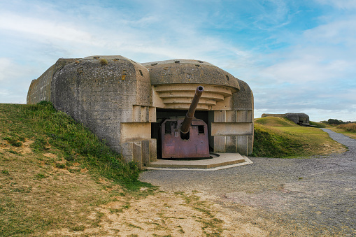 Normandy, France, September 02, 2019: Looking at a 150mm canon of the Longues-sur-Mer artillery battery wich was constructed during the World War II by germans army near the french village of Longues-sur-Mer. The battery was sited on a 60 m (200 ft) cliff overlooking the north sea and formed a part of Germany's Atlantic Wall coastal fortifications. But it couldn´t prevent the Allied landing beaches of Gold and Omaha and shelled both beaches on D-Day (6 June 1944).