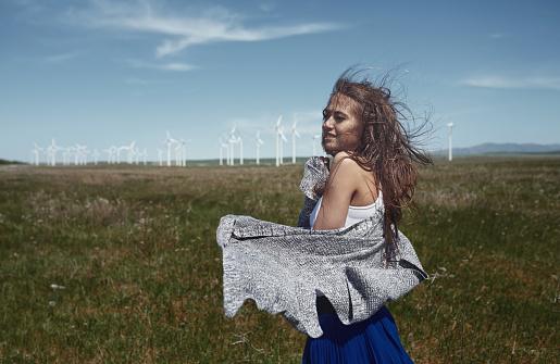 Woman with long tousled hair next to the wind turbine with the wind blowing