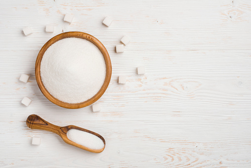 White sugar in bowl and scoop on wooden table background