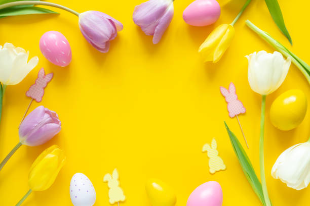 istock Greeting card with text. Multicolored easter eggs and tulips on yellow background. Copy space for your text 1365824855