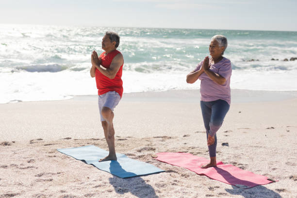 istock Senior biracial couple practicing tree pose yoga on exercise mats at beach during sunny day 1365835389