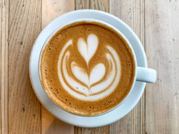 A mug of flat white coffee on a wooden background. Coffee art. Heart flower  shape latte art