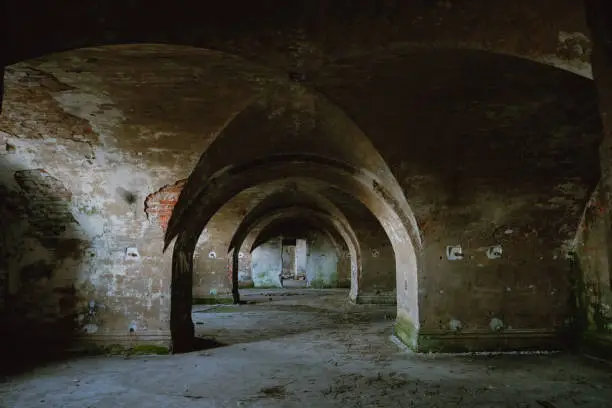 Photo of Abandoned building. The interior of the old building with rounded arches and unusual ceiling vaults. Shabby old brick, sprinkled with plaster, grundy interior decoration with green fungus on the walls