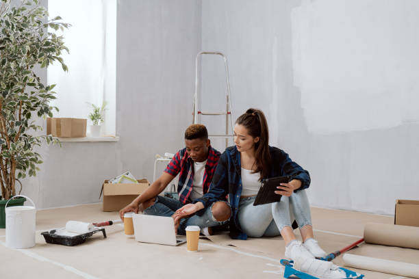 istock Interior designers construction managers architects work in newly constructed apartment building apartment renovation young woman and co-worker sit on floor with mugs of coffee laptop tablet plan 1365838590