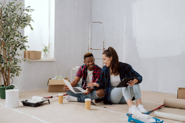 istock Smiling interior designers construction managers architects work in newly constructed apartment building flat renovation young woman and co-worker sit on floor with mugs of coffee laptop tablet plan 1365838611