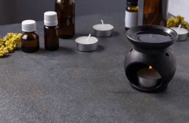 Essential oil burner,fire candle,aroma steam and bottles of oil,herbal ingredients on the grey surface.Empty space