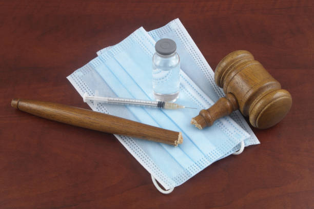 istock Broken judge gavel with vaccine bottle syringe and face masks on table. 1365841571