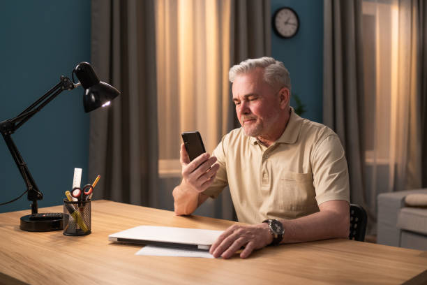 istock A gray-haired man learns to use a telephone. An elderly man gets acquainted with his new smartphone. A grandfather calls his grandchildren and sends text messages. An elderly man makes company phone calls 1365841854