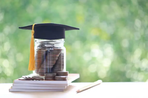 Photo of Graduation hat on coins money in the glass bottle on natural green background, Saving money for education concept