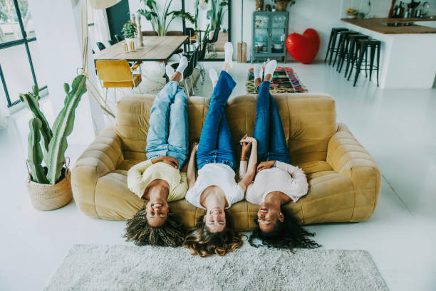 tres jóvenes hispanas sonriendo felices acostadas en el sofá de casa - adolescentes multirraciales de pie boca abajo en el sofá divirtiéndose juntas en la sala de estar - estilo de vida feliz y concepto femenino - little girls only fotografías e imágenes de stock