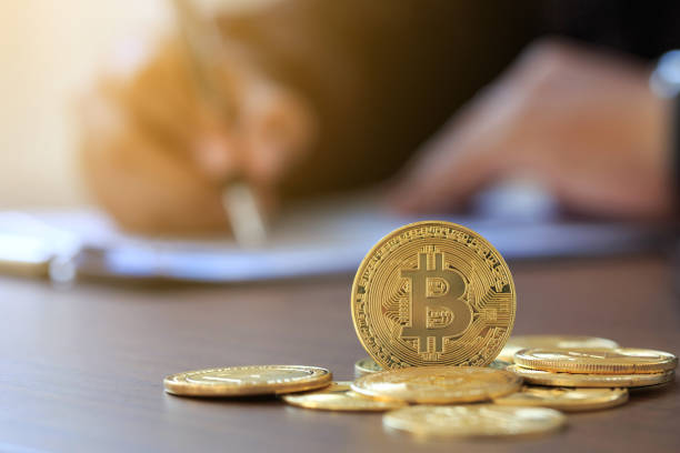 Bitcoin on wooden table and man signing individual income tax return form 1040. in background. tax for the trading of crypto-currencies.The time to pay taxes concept. stock photo