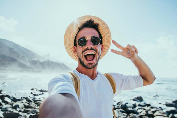 Happy handsome man taking selfie outside - Smiling guy having fun on the beach - Mobile, travel and people lifestyle concept stock photo