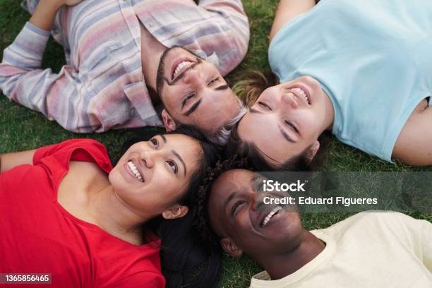 Young Friends Smiling Lying Together On Grass In Park Focus On Latin American Girl Stock Photo - Download Image Now