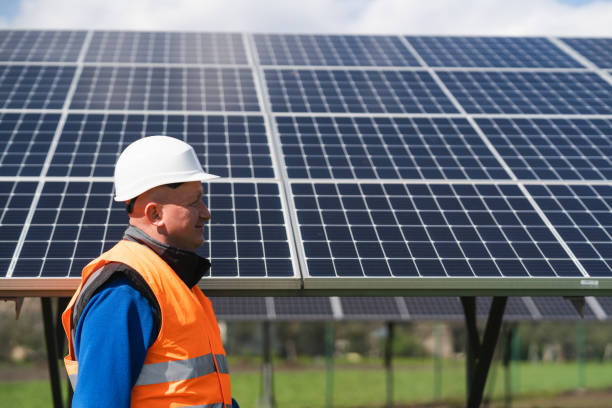 istock Engineer in work clothes and helmet walks through a solar power plant against the backdrop of panels 1365856777