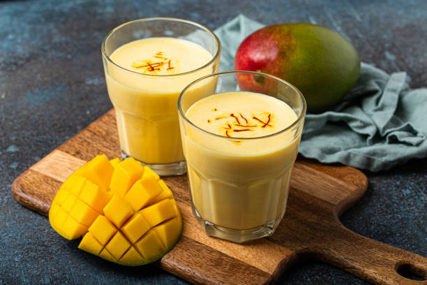 buvez du lassi à la mangue dans deux verres sur une table en béton rustique avec du manfo fraîchement mûr coupé d’en haut - mangue photos et images de collection