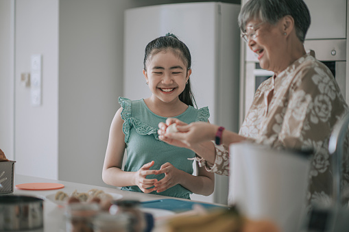 Asian Chinese Senior woman showing and teaching her granddaughter preparing chinese dumpling in kitchen during weekend leisure time