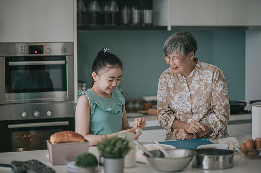 Asian Chinese young girl learning from her grandmother preparing chinese dumpling in kitchen during weekend leisure time